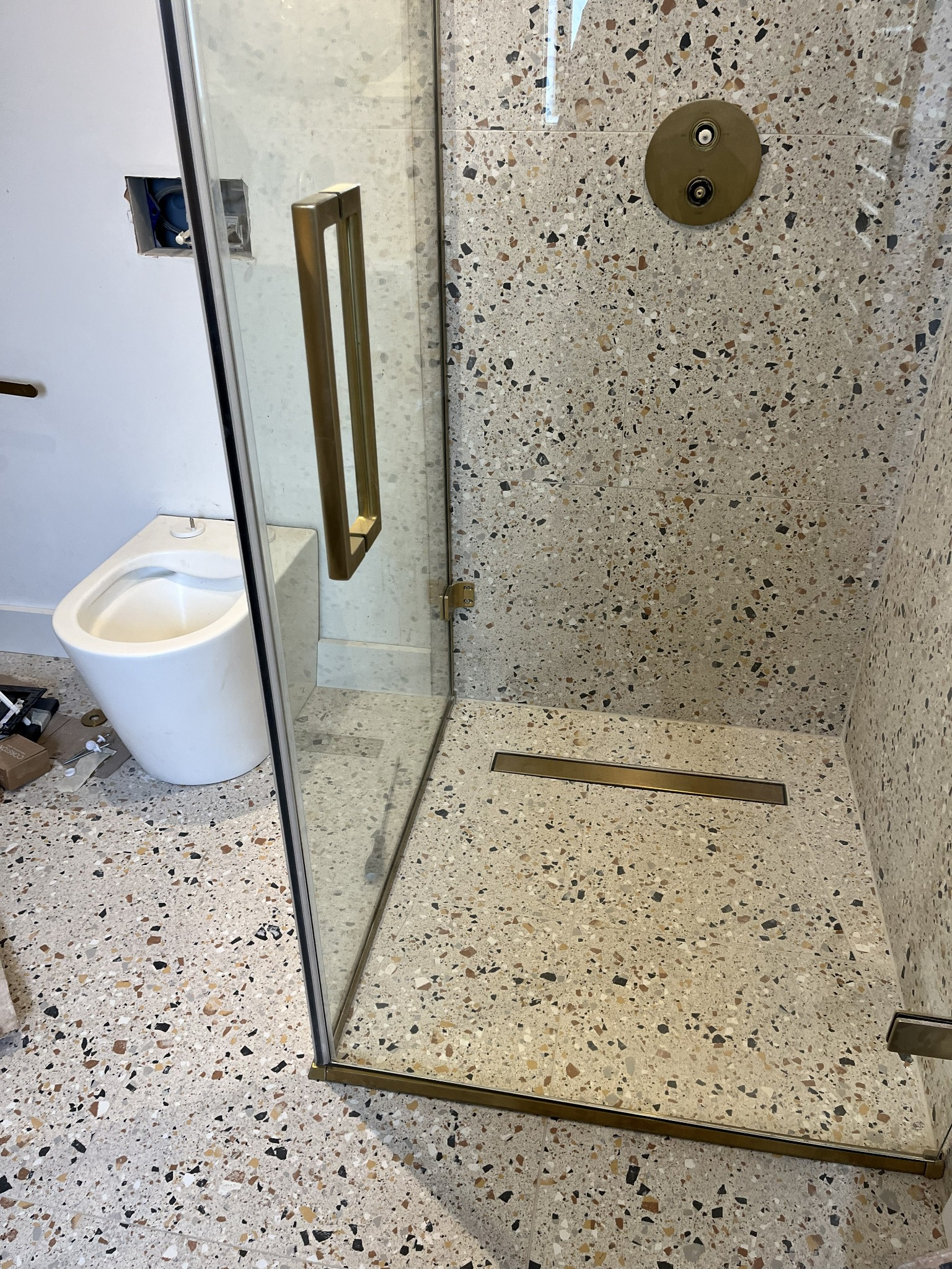 Terrazzo-style walk-in shower with brushed brass fittings and linear drain